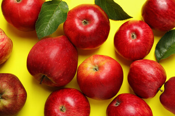 Ripe red apples and green leaves on yellow background, flat lay
