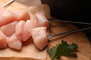 Fondue forks, raw meat pieces and parsley on table, closeup