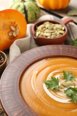 Delicious pumpkin soup with seeds and parsley in bowl on table, closeup