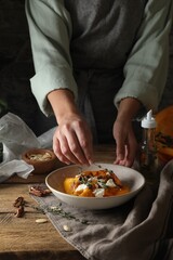 Woman adding aromatic thyme onto freshly baked pumpkin slices with cheese and pecans at wooden table, closeup