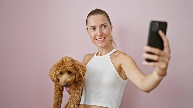 Young caucasian woman with dog smiling hugging using smartphone over isolated pink background