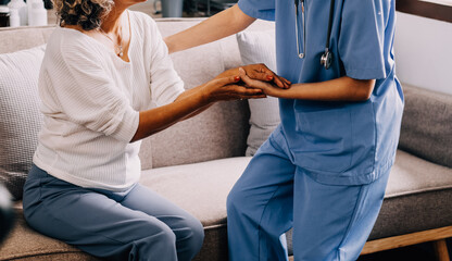 Obraz premium Happy young female nurse provide care medical service help support smiling old grandma at homecare medical visit, lady carer doctor give empathy encourage retired patient sit on sofa at home hospital
