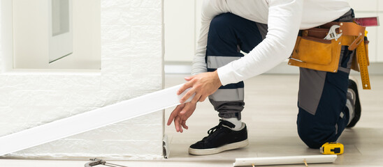 The foreman installs a plastic outer corner for the floor plinth during the repair of the floor -...