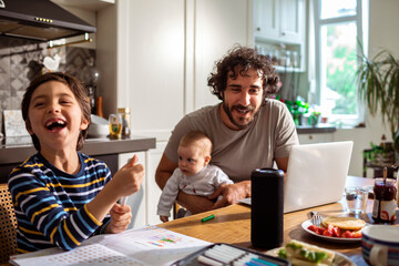Joyful family moment as son laughs during breakfast with multitasking dad