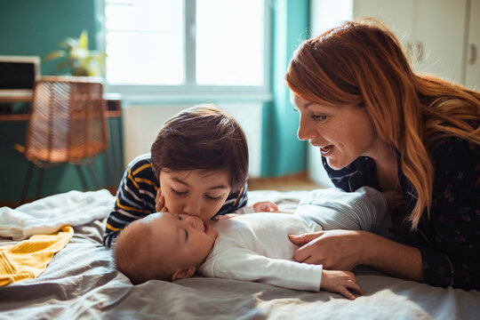 Tender moment between a mother, her elder son, and newborn in a sunlit room