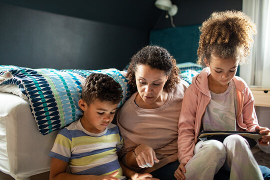 Young mother using the tablet with her kids in the bedroom - Powered by Adobe