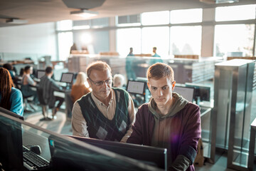Teacher helping a student on a computer in the high school library