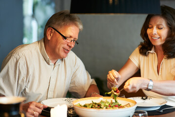 Mature couple, eating together at table with food and love in marriage with happiness in home. Lunch, old man and woman with smile, diet and salad for dinner in house with kindness, bonding and meal.