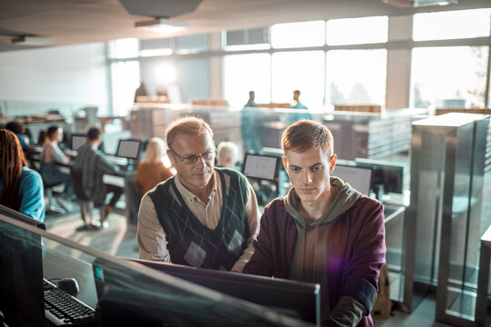 Teacher helping a student on a computer in the high school library