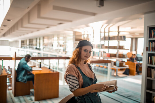 Stylish young woman with a beret exploring literature in a sunlit library