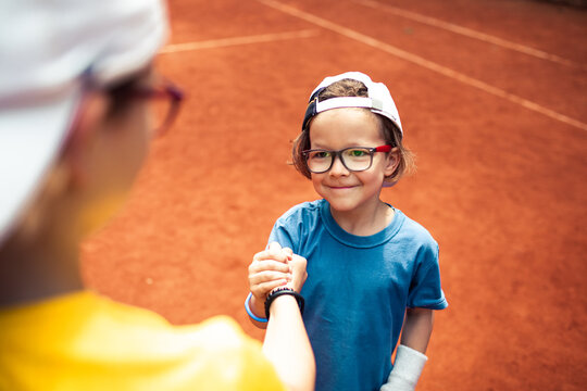 Young boy with glasses offers a handshake on the tennis court
