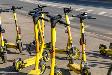 Several yellow rental electric scooters on a city street. The group of push electricscooters for...