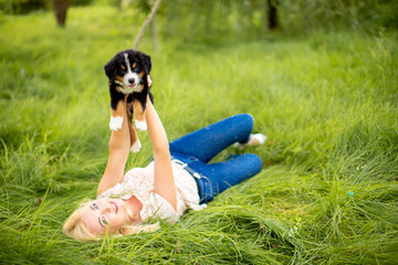 A beautiful girl with a dog sits in the park on the grass. Love to the animals. Home pet on a walk. Animal protection. Bernese mountain dog puppy.