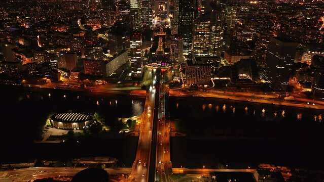 High angle view of traffic on roads in night city. Tilt up reveal of modern urban borough La Defense with skyscrapers. Paris, France