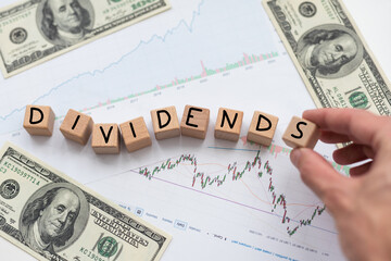 Dividends payment concept with letters on wooden cubes. Still life of office workplace with supplies. Flat lay white surface with laptop, notepad and financial report. Capital savings and investment