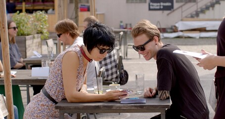 Couple using his phone during the date. Checking messages, browsing the internet, or using it as a conversation starter or to share something interesting with girl. People lifestyle.