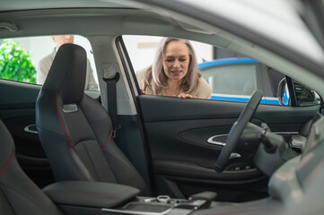 Gray-haired woman looks through a car window in a car dealership.