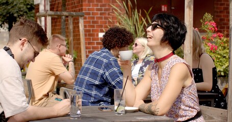 Young woman is enjoying a cup of coffee during conversation at city cafe. Vibrant urban energy. They exchange thoughts, share stories, and laugh freely. Hub of social interaction and human connection.