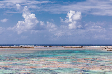 French Polynesia Tikehau atoll with pink coral reef lagoon and clouds over a blue sky.