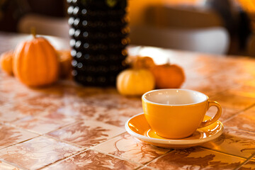 A yellow cup of coffee or tea on the table with pumpkin autumn decoration in a coffee shop