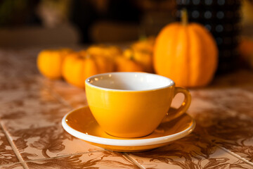 A yellow cup of coffee or tea on the table with pumpkin autumn decoration in a coffee shop
