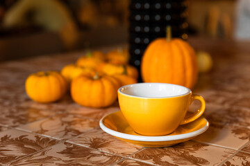 A yellow cup of coffee or tea on the table with pumpkin autumn decoration in a coffee shop