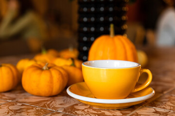 A yellow cup of coffee or tea on the table with pumpkin autumn decoration in a coffee shop