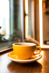 A yellow porcelain cup of coffee on the wooden windowsill