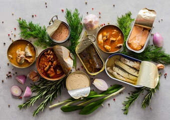 Different open tin cans with canned fish among spices and herbs, canned salmon and mackerel, sprat...
