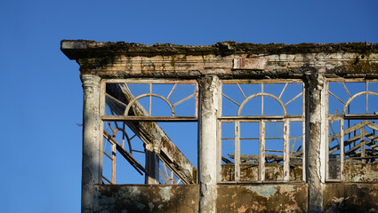 Window of a ruined house facade with old and broken glass in a stone wall in a lost place in Batumi. Vintage background with traces of destruction and demolition. blue sky backdrop.