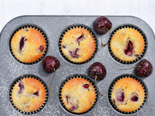 Baking muffins with cherries. Baking tray with paper cases with freshly baked muffins and fresh fruits, sprinkled with powdered sugar