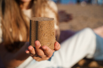 A girl holds a sand cake on her hand on the beach
