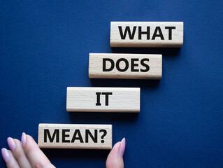 What does it mean symbol. Wooden blocks with words What does it mean. Beautiful deep blue background. Businessman hand. Business and What does it mean concept. Copy space.