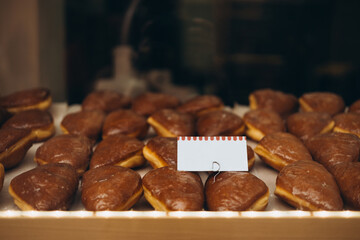 A showcase with mini cakes in a cafe. Delicious sweets in the refrigerator. Price tag. Hanukkah doughnuts with jelly and sugar powder, mock up