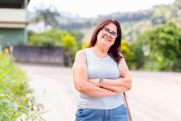 Mature Brazilian woman smiling and looking at the camera with her arms crossed, showing a positive...