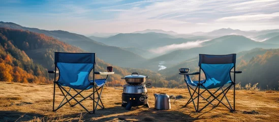 Papier Peint photo Lavable Camping Active travel concept with two blue camping chairs gas burner kettle stand amidst beautiful autumn mountains