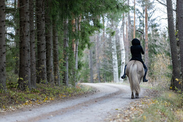 Reaper riding on gravel road in Autumn scenery.  Ghost rider. Icelalandic horse. Halloween