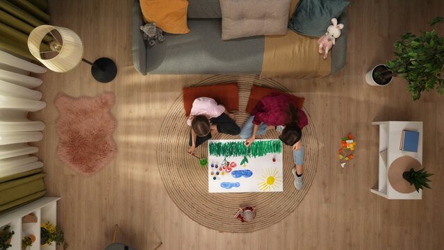 In the picture from above sit on the floor a woman and a child they together draw on paper. They communicate, spend time together. Theres a couch with toys next to it, paint on the floor.