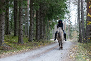 Reaper riding on gravel road in Autumn scenery.  Ghost rider. Icelalandic horse. Halloween