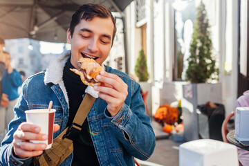 Young happy man having breakfast with coffee and croissant sitting at outdoor cafe in European city.