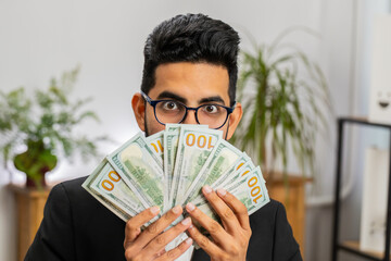 Shocked Rich Indian businessman working counting money cash, calculate earnings income profit lottery jackpot game winner at home office workplace. Professional manager freelancer man. Business people