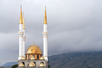 A fragment of a mosque with white minaret towers and gilded domes. The background of the mountain...