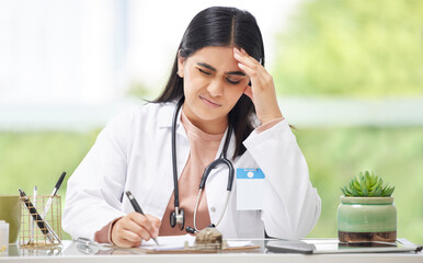 Headache, stress and burnout medical doctor working in hospital, looking in pain and writing in a book while sitting in office at clinic. Tired, unhappy and professional female healthcare worker