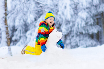 Fototapeta na wymiar Child making snowman. Kids play in snow in winter