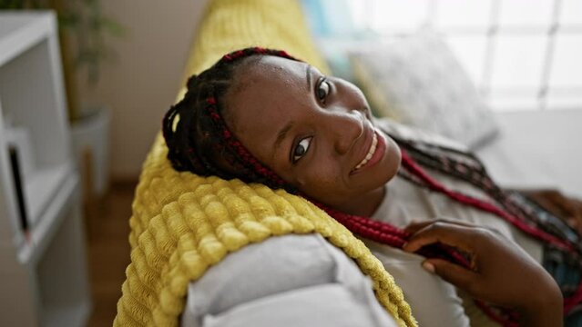 Cheerful african american woman enjoying a bout of contagious laughter while confidently relaxing on her home's comfy sofa
