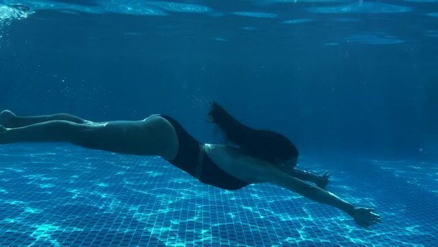 Underwater footage of a woman swims in clear blue water in the pool