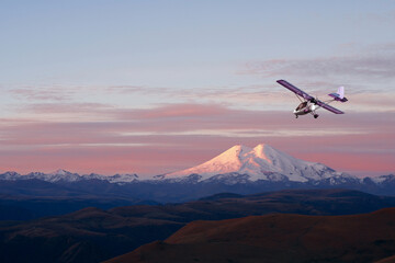 Fototapeta na wymiar A picturesque panoramic view at dawn of a snow-capped volcano and a light two-seater plane in flight. Copy space.