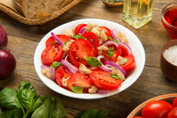 Italian salad Panzanella tomatoes pieces of bread and onions in a salad bowl on a rustic wooden table with ingredients. - 671813822
