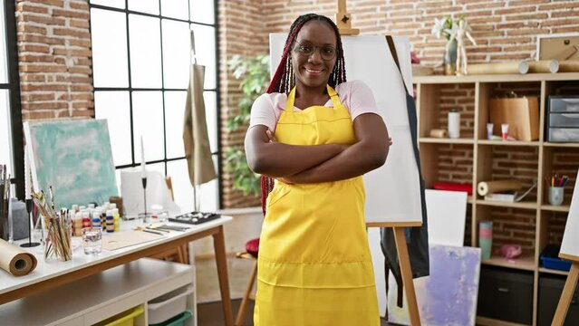 Confident african american woman artist, smiling, standing with arms crossed in art studio