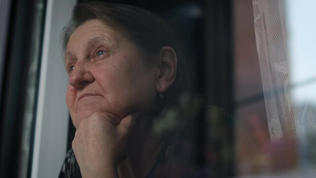 Pensive sad elderly woman at the window, close-up
